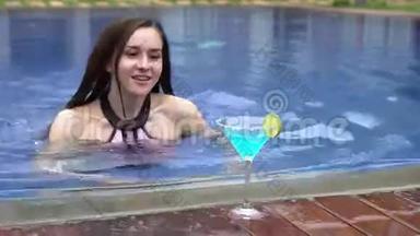 美丽的女孩在游泳池里游泳，喝蓝色的coctail。